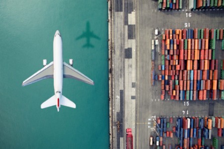 EY - Plane flying over water and cargo containers